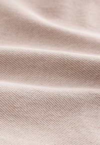 Tissu beige doux avec une texture fine en côtes diagonales et des plis légers créant des ombres et des reflets.