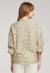 Blouse à collier en tissu avec un motif répétitif vert, rose et blanc. Présente des manches roulées et un dos avec un empiècement.