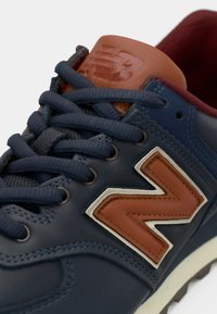 Blue leather sneaker featuring brown and cream accents, textured laces, and a prominent logo on the side.