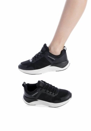 Par de zapatillas deportivas en negro y blanco, una usada en el pie, con parte superior de malla de punto y suela gruesa acolchada.