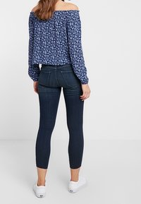 Dark blue, stretchy skinny jeans with back pockets paired with a floral off-the-shoulder top, featuring a gathered texture and long sleeves.