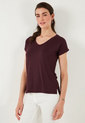 Camiseta de manga corta en color burdeos con cuello en V, hecha de tejido ligero, que presenta aberturas laterales y mangas enrolladas para facilitar el movimiento.