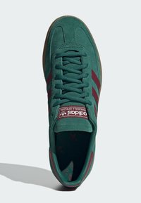 Zapatillas de gamuza verde con rayas marrón, material texturizado y suela de goma marrón. Presenta una lengüeta acolchada con detalle del logo.