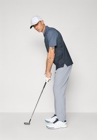 Golf attire featuring a dark blue polo shirt, light gray pants, white golf shoes with blue accents, and a white cap. Player holding a golf club.