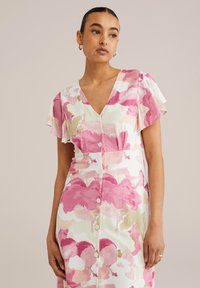 Robe florale rose et crème avec des manches courtes volantes, un décolleté en V et une fermeture à boutons sur le devant. Fabriquée en tissu léger avec une texture douce.