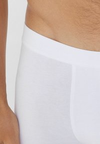 Białe bawełniane majtki, charakteryzujące się gładką teksturą, elastycznym pasem i dopasowanym krojem. Materiał wydaje się miękki i elastyczny dla większego komfortu.