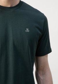 Dark green short-sleeve T-shirt made of cotton, featuring a small white logo "M O P" on the left chest area. Smooth texture, classic crew neck design.