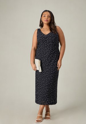 Ärmelloses, navyblaues Kleid mit weißen Polka-Dots, V-Ausschnitt, gerade Silhouette, mittellang. Kombiniert mit einer Perlen-Clutch und Riemchen-Sandalen.