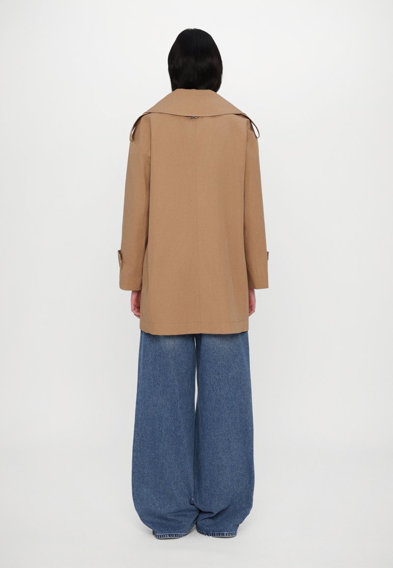 Brązowy płaszcz wełniany z dużym kołnierzem, z guzikami na rękawach i prostym krojem. Połączony z szerokimi, jasnoniebieskimi dżinsami.