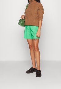 Brun randig höghalsad tröja, gröna shorts med snörning, svarta vadderade slip-on skor och en mönstrad grön och svart handväska.