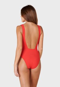 Maillot de bain une pièce rouge avec de larges bretelles et un dos plongeant. Texture lisse et design ajusté, adapté à diverses activités aquatiques.