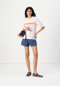 Lichtroze grafische t-shirt met een kokosnootillustratie en oranje tekst, gecombineerd met denim shorts en een zwarte handtas. Dierenprint ballerina's.