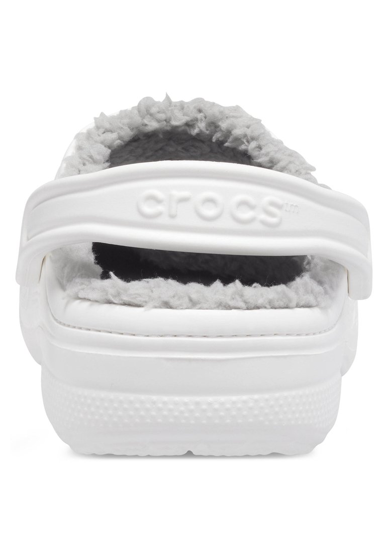 Witte Crocs met een grijze vachtvoering en een witte verstelbare hielband met het "crocs" logo, getoond vanachter.