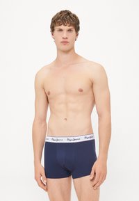 Boxeri scurți de culoare bleumarin cu un elastic alb cu logo. Fabricul pare neted, iar designul este ajustat, evidențiind un stil minimalist.