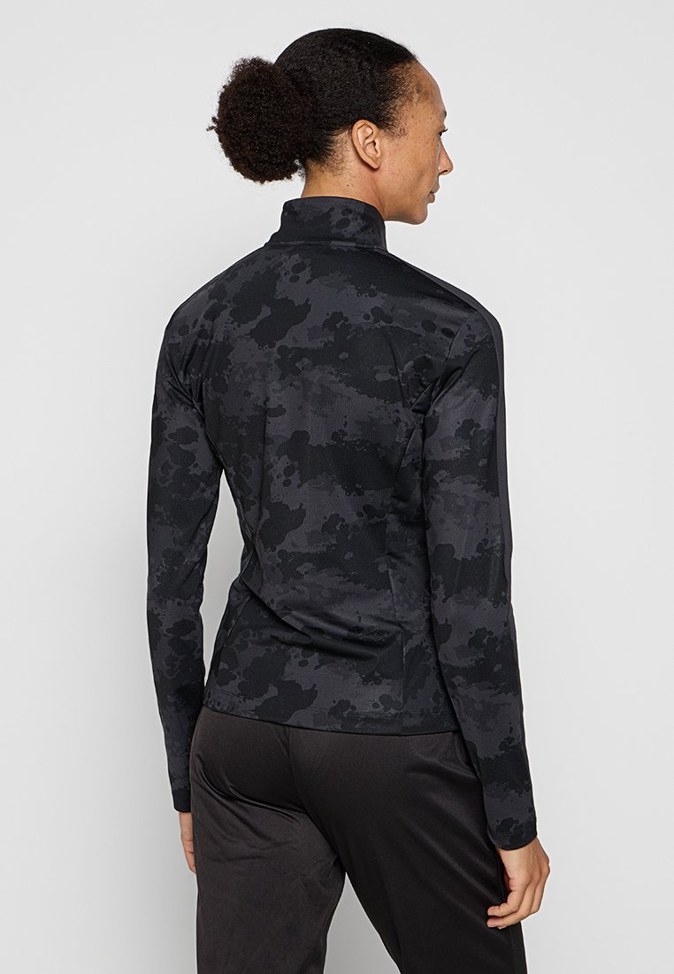 Černá dlouhá sportovní bunda s texturovaným maskáčovým vzorem, vysokým límcem a přiléhavým střihem. Materiál vypadá lehce a pružně.
