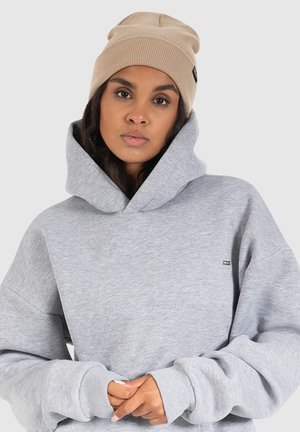 Heather grå hoodie med en stor hætte og manchetter, suppleret med en beige strikket beanie. Har et lille logo på fronten.