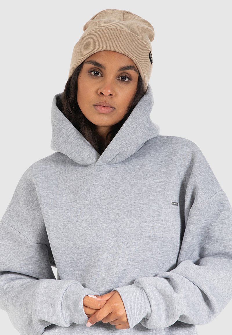Heather gray hoodie with a large hood and cuffed sleeves, complemented by a beige knit beanie. Features a small logo on the front.