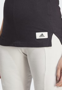 Juodas medvilninis topas su baltu Adidas logotipu apatinėje dalyje, su šoninėmis plyšio detalėmis. Derinamas su šviesiai raibomis leginsomis.
