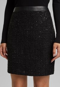 Svart minikjol i ett texturerat tyg med paljetter, en slät lädermidja och en åtsittande design som framhäver ett polerat utseende.