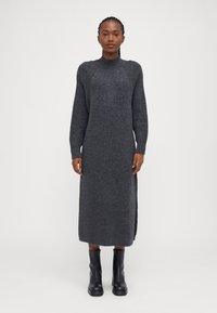 Μακρύ, σκούρο γκρι πλεκτό φόρεμα με ψηλό λαιμό και ριμπ λεπτομέρειες. Διαθέτει πλαϊνές σχισμές και συνδυάζεται με μαύρες μπότες μέχρι το γόνατο.