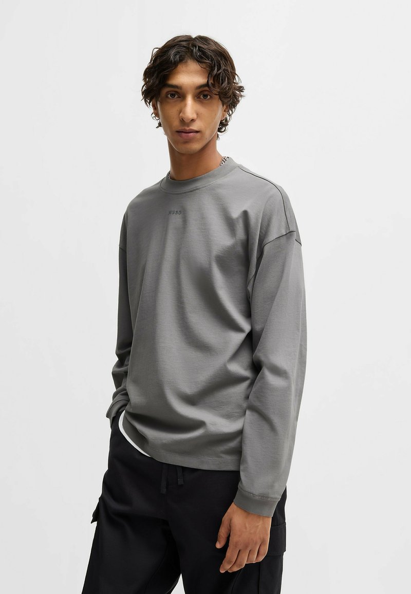Sweatshirt à manches longues gris en tissu doux, avec un col rond, des épaules tombantes et un logo discret sur la poitrine.