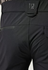 Pantalones de tela elástica negra con un diseño ajustado, que cuentan con una cinturilla plana y un pequeño bolsillo trasero, resaltando su textura suave y su marca discreta.