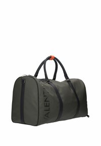 Sac de sport vert foncé avec poignées et sangles noires, une petite étiquette orange, et le nom de la marque embossé partiellement visible sur le côté.