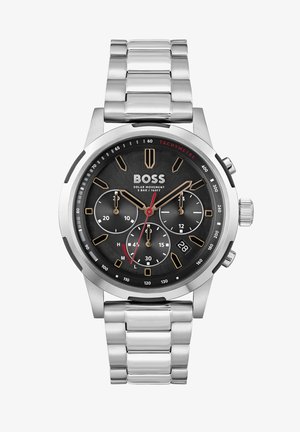 Reloj cronógrafo de acero inoxidable plateado con una esfera negra, acentos dorados, manecillas rojas, tres subesferas y pantalla de fecha. Movimiento solar.