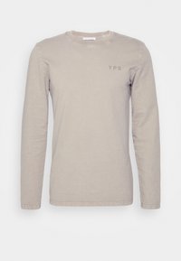 Camiseta de manga larga y cuello redondo en algodón de color beige claro con un sutil logo "YPS" en el pecho. Textura suave y ajuste casual.
