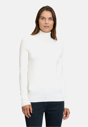 Maglione bianco a collo alto in tessuto a coste, design aderente, maniche lunghe e una texture liscia, abbinato a pantaloni scuri.