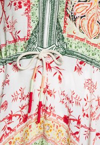 Detailní záběr na látku s květinovými vzory v červené, zelené a žluté barvě a bílou šňůrkou se barevnými konci svázanými do mašle.