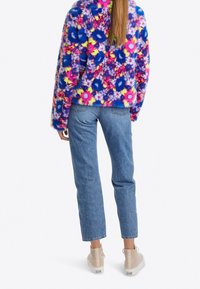 Miękki, kolorowy sweter z kwiatowymi wzorami w różu, niebieskim i żółtym; w połączeniu z jasnoniebieskimi jeansami o prostych nogawkach i beżowymi tenisówkami.