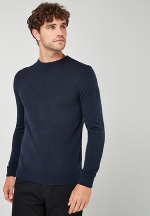 Pull à col rond marine en tricot doux avec des manches longues et des poignets côtelés. Design simple sans motifs ni embellissements.