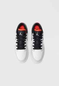 Λευκά και γκρι δερμάτινα sneakers με μαύρα κορδόνια, μαύρες λεπτομέρειες στη γλώσσα και κόκκινη επένδυση. Διαθέτουν διάτρητη μύτη και λογότυπο στα πλάγια.