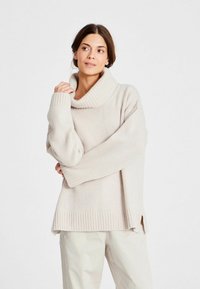 Lichtbeige oversized trui met een brede geribde col, drop schouders en geribde manchetten. Zijsplitten aan de onderkant voor extra comfort.