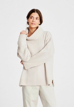 Pulover oversized de culoare bej deschis, cu guler înalt cu nervuri late, umeri lăsați și manșete cu nervuri. Fante laterale la tiv pentru un plus de confort.