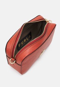 Borsa in pelle rossa con finitura testurizzata, presenta una zip dorata e un'etichetta interna con il marchio, mostrando una forma rettangolare.