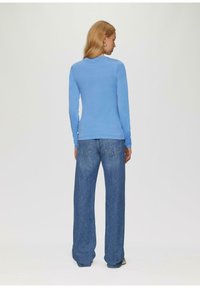Langärmliges hellblaues Oberteil mit rundem Ausschnitt, kombiniert mit locker sitzenden blauen Jeans aus Denim mit Gesäßtaschen und leicht ausgestellten Beinenden.