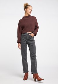 Bordeauxrotes, kurz geschnittenes Strickoberteil mit hohem Kragen und lockeren Ärmeln; kombiniert mit grauen, hoch taillierten, geraden Jeans und braunen, hohen Stiefeletten.