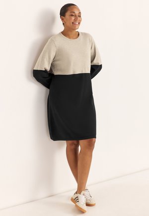 Sweatshirt-Kleid mit beigem Oberteil und schwarzem Unterteil, langen Ärmeln und lockerem Schnitt; kombiniert mit hellen Sneakers.