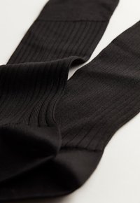 Sorte ribbede strømper lavet af strækbart materiale med en blød tekstur og sømløs design. Har en glat talje og gradvis opacitet.