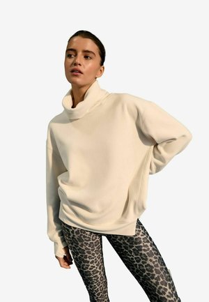 Cremefarbener, übergroßer Pullover mit hohem Kragen. Kombiniert mit eng anliegenden schwarzen Leggings mit Leopardenmuster.