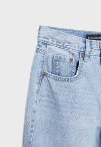 Jeans de mezclilla azul claro con una cintura alta, herrajes de latón, cinco bolsillos y una textura ligeramente desteñida.