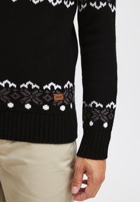 Black knitted sweater featuring a white and gray geometric pattern on the bottom, ribbed cuffs, and a leather label with "ISOLID."
