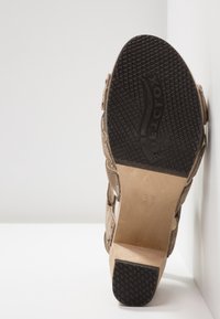 Sandale en daim marron avec un talon épais, semelle en caoutchouc texturé noir, découpes latérales et détails de couture subtils. Taille 37 indiquée sur la base.