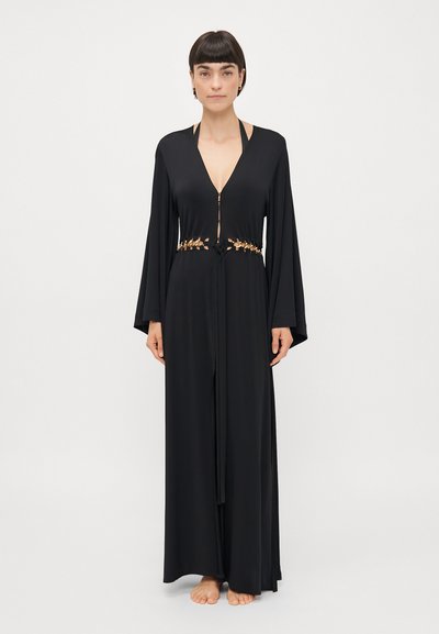 Lunga veste nera con scollatura a V profonda, maniche a campana e vita cin cin che presenta dettagli in foglia dorata e chiusura frontale con zip.