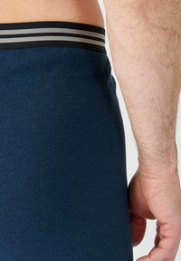 Boxer shorts ajustados de color azul marino con una cintura elástica de rayas en negro y gris. El material tiene una textura suave con un acabado liso.
