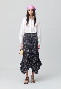 Camisa blanca de botones con detalles de encaje, falda negra de varias capas con patrón floral blanco, dobladillo con volantes y un pequeño bolso de mimbre. Bufanda rosa como tocado.
