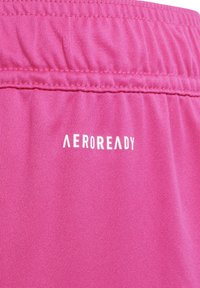Close-up van roze stof met geplooide stiksels en het witte "AEROREADY" logo bedrukt op het gladde, getextureerde sportmateriaal.