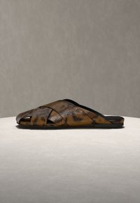 Sandale à enfiler en cuir motif serpent marron et noir avec des brides croisées et une semelle plate sur une surface claire.